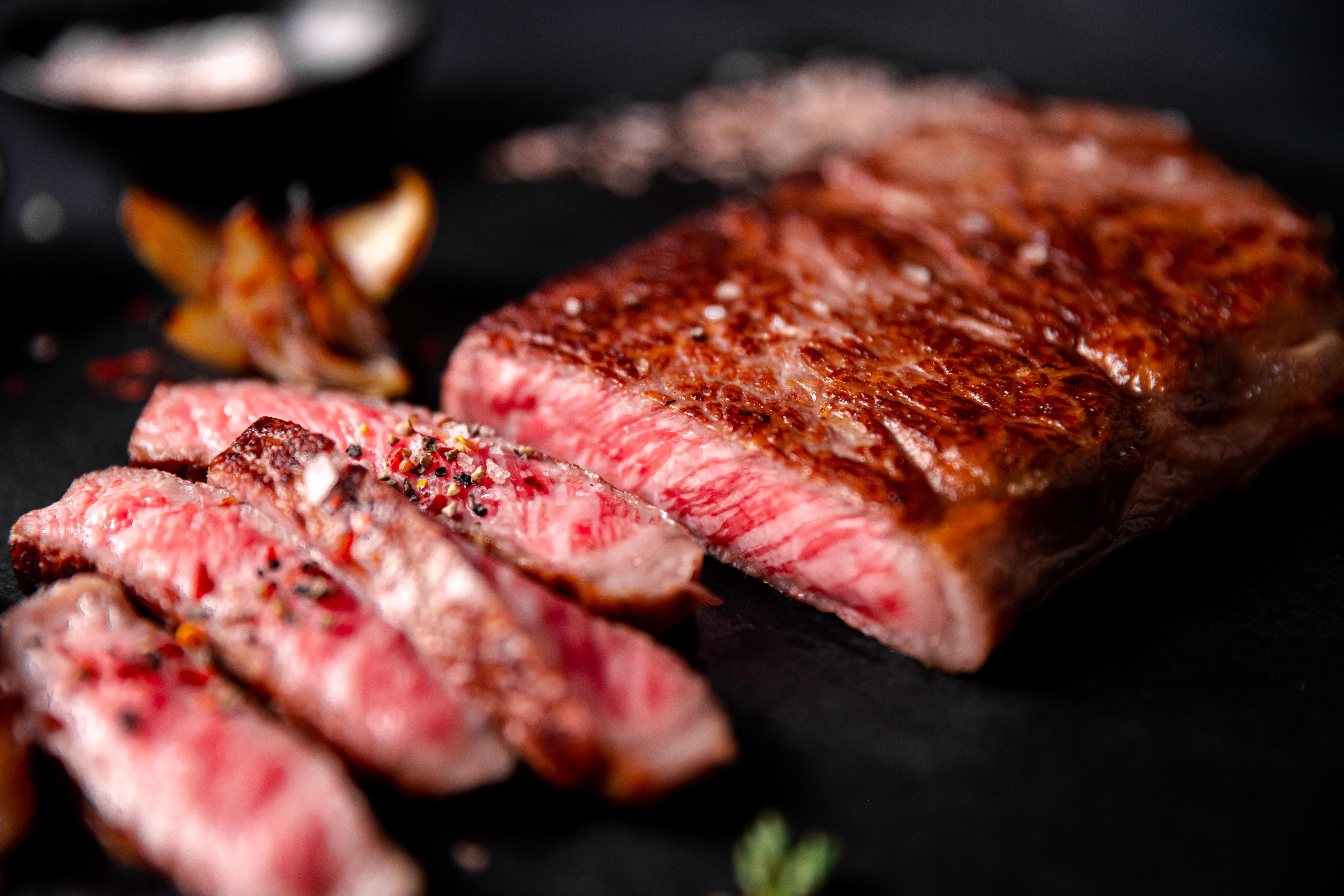 Sliced, seared A5 Olive Wagyu New York strip on a dark plate