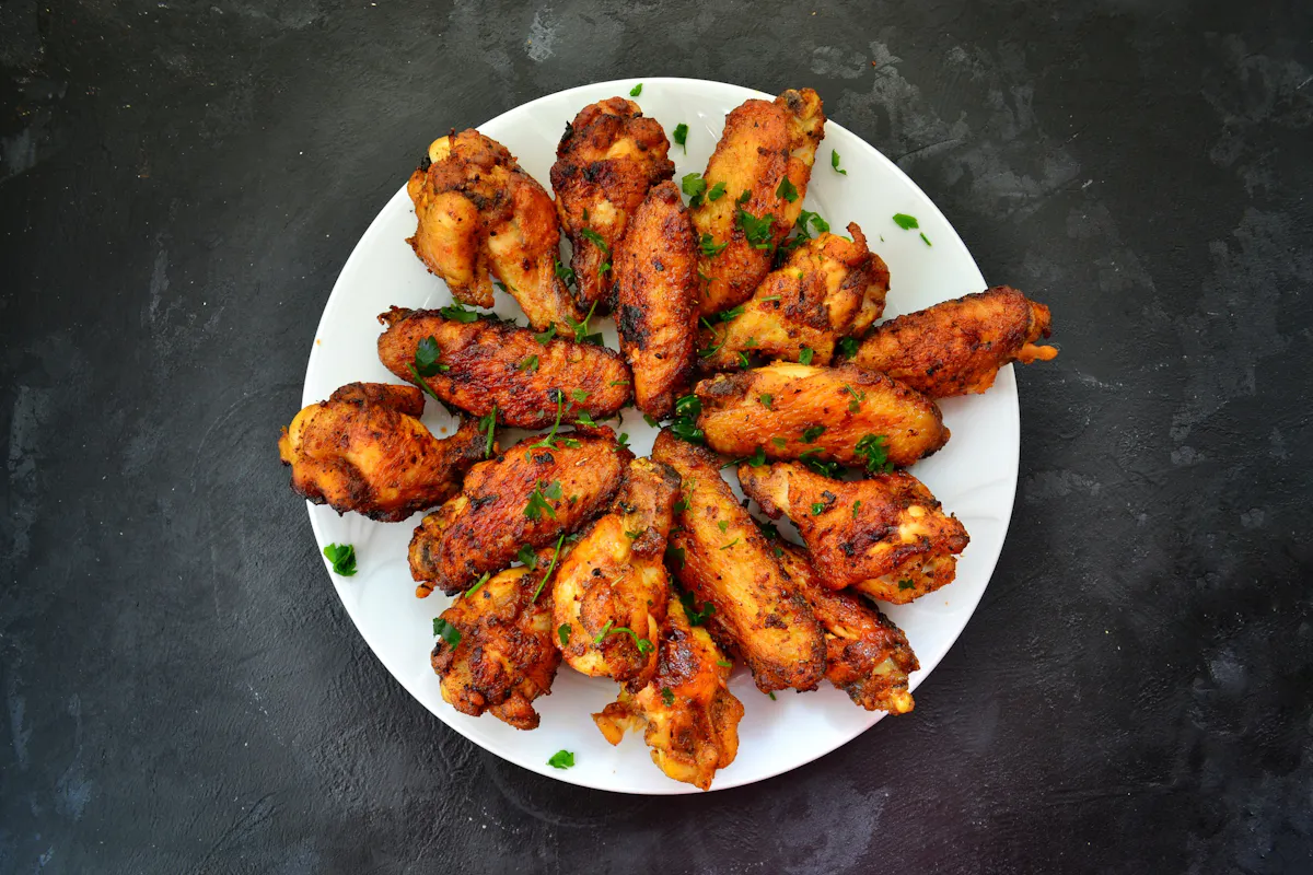 A white plate of seasoned roasted chicken wings with chopped herbs on dark stone