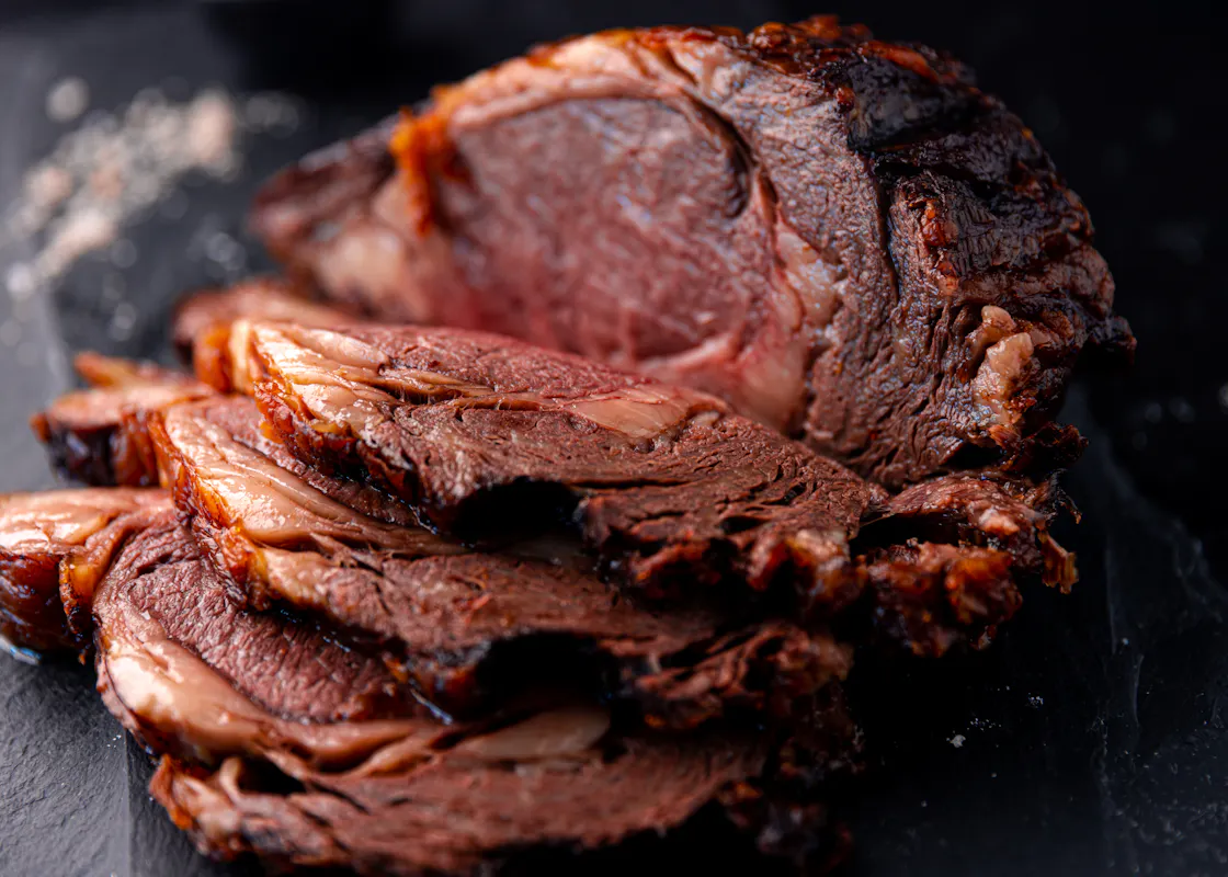 A deeply crusted, sliced ribeye roast on dark slate