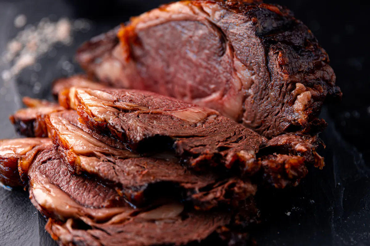 A deeply crusted, sliced ribeye roast on dark slate