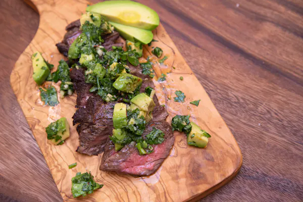 Grilled skirt steak topped with avocado chimichurri on a wooden board