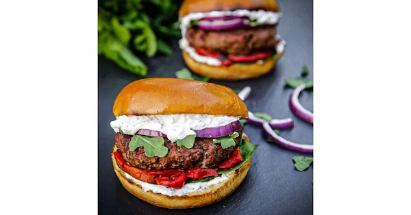 A lamb burger topped with tzatziki, red onion, greens and roasted red peppers