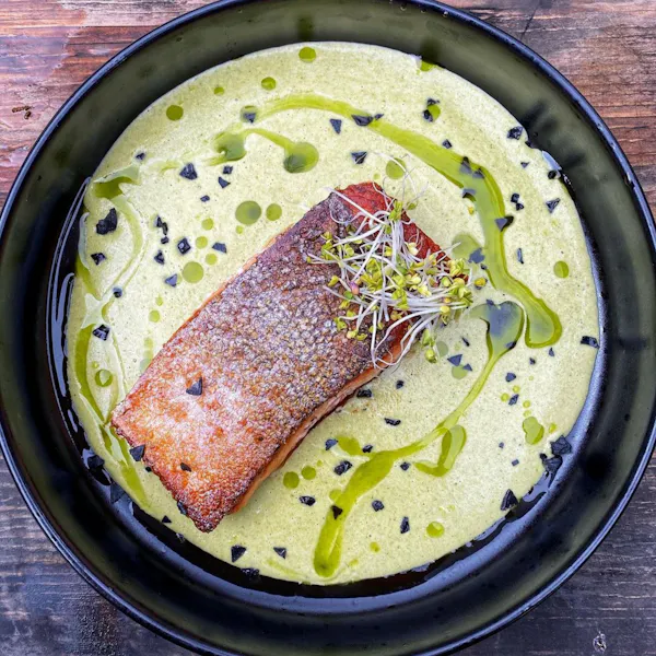 Seared Ōra King salmon in a black bowl with green sauce
