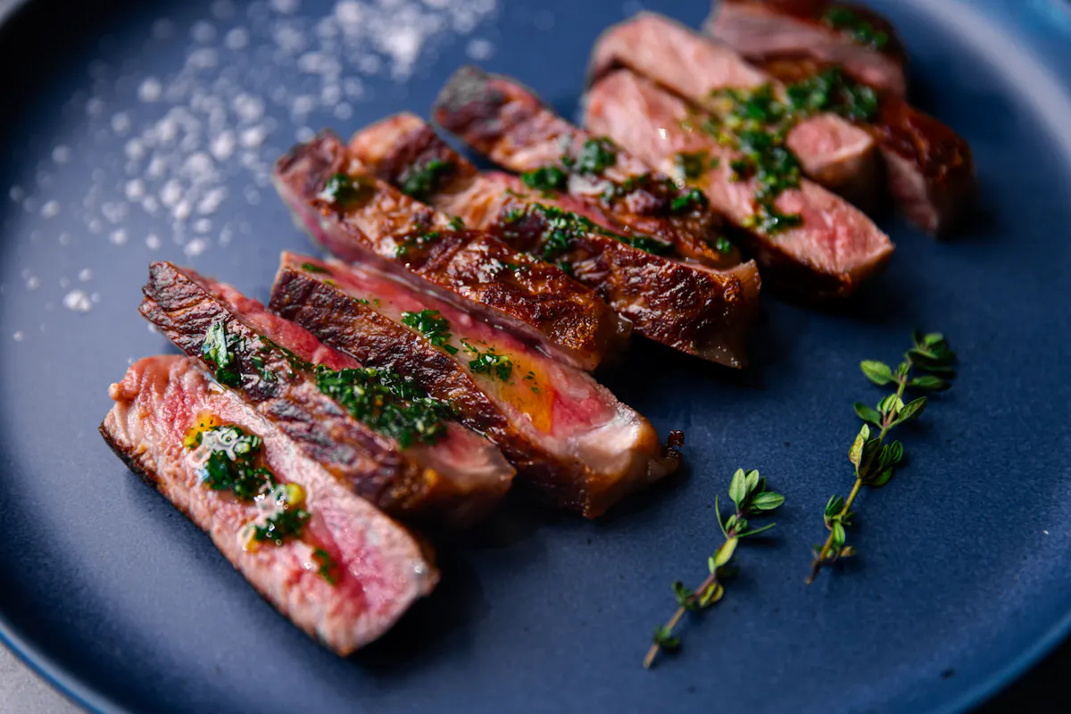 Sliced, seared New York strip with herb sauce and thyme on a dark blue plate