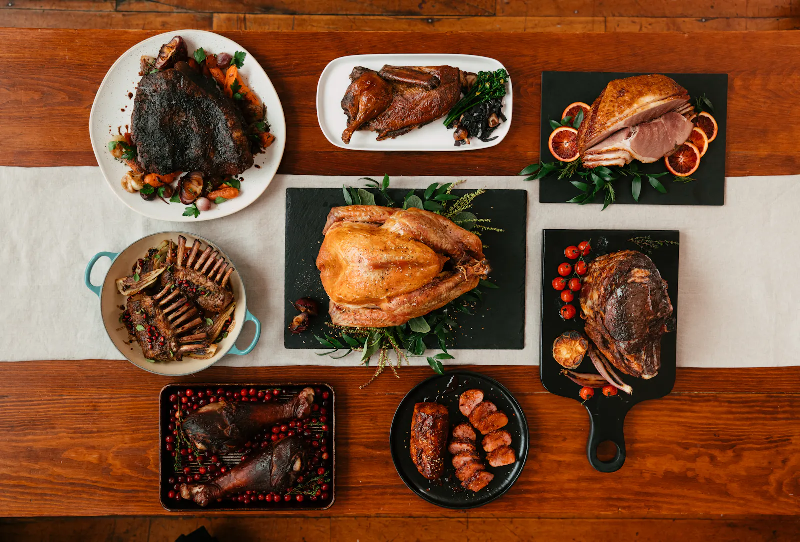 A Thanksgiving table with a roast turkey, rib roast, ham, rack of lamb and duck