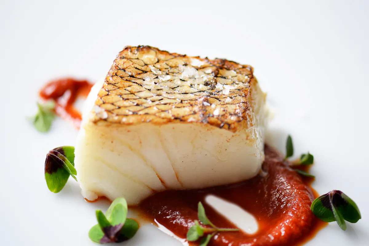 A seared Chilean sea bass fillet with crisp skin on red pepper sauce and microgreens