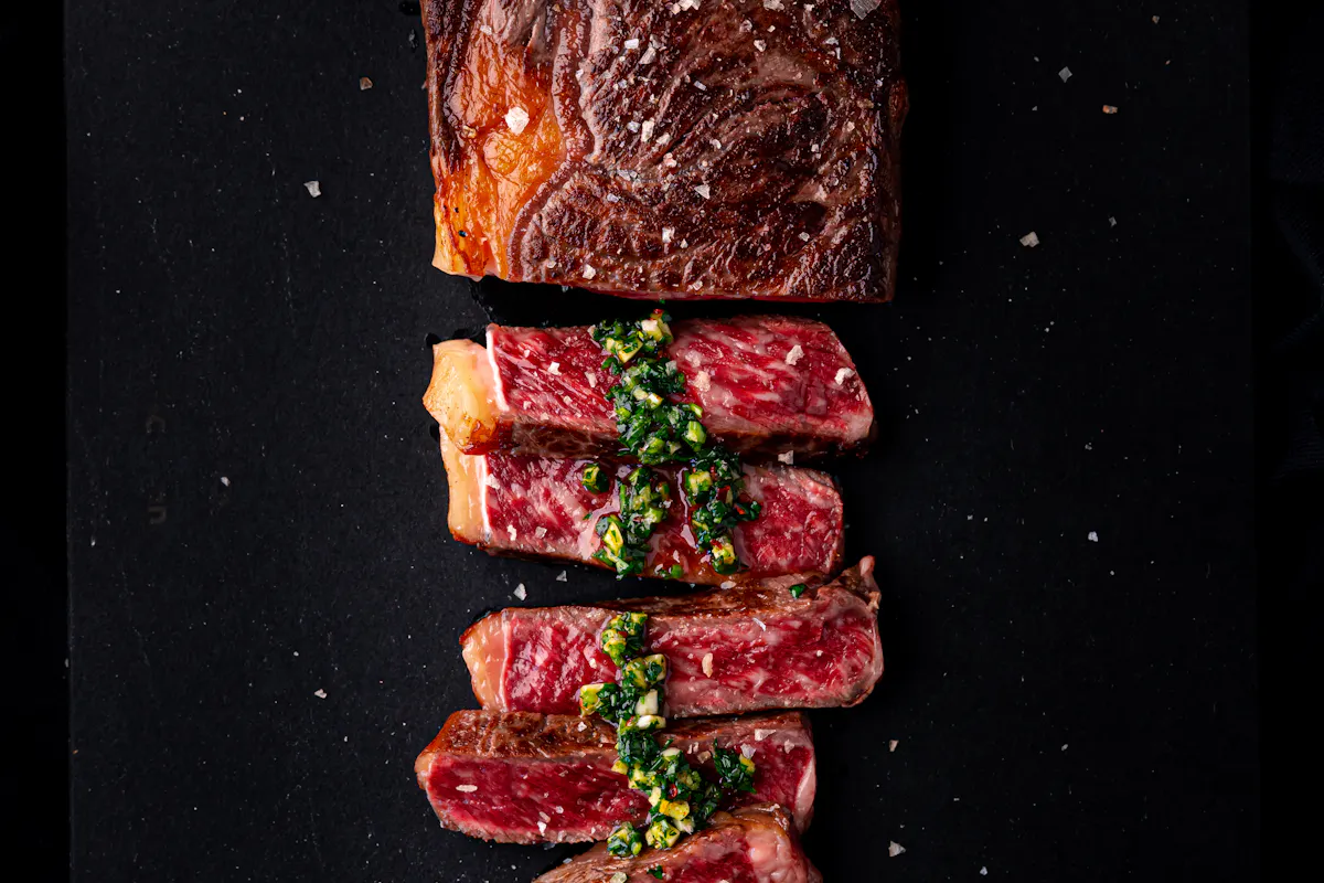 A seared, deeply marbled Wagyu ribeye sliced on a black board with herb sauce