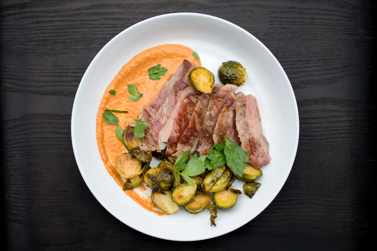 Sliced Ib&eacute;rico pork pluma with romesco sauce and roasted Brussels sprouts