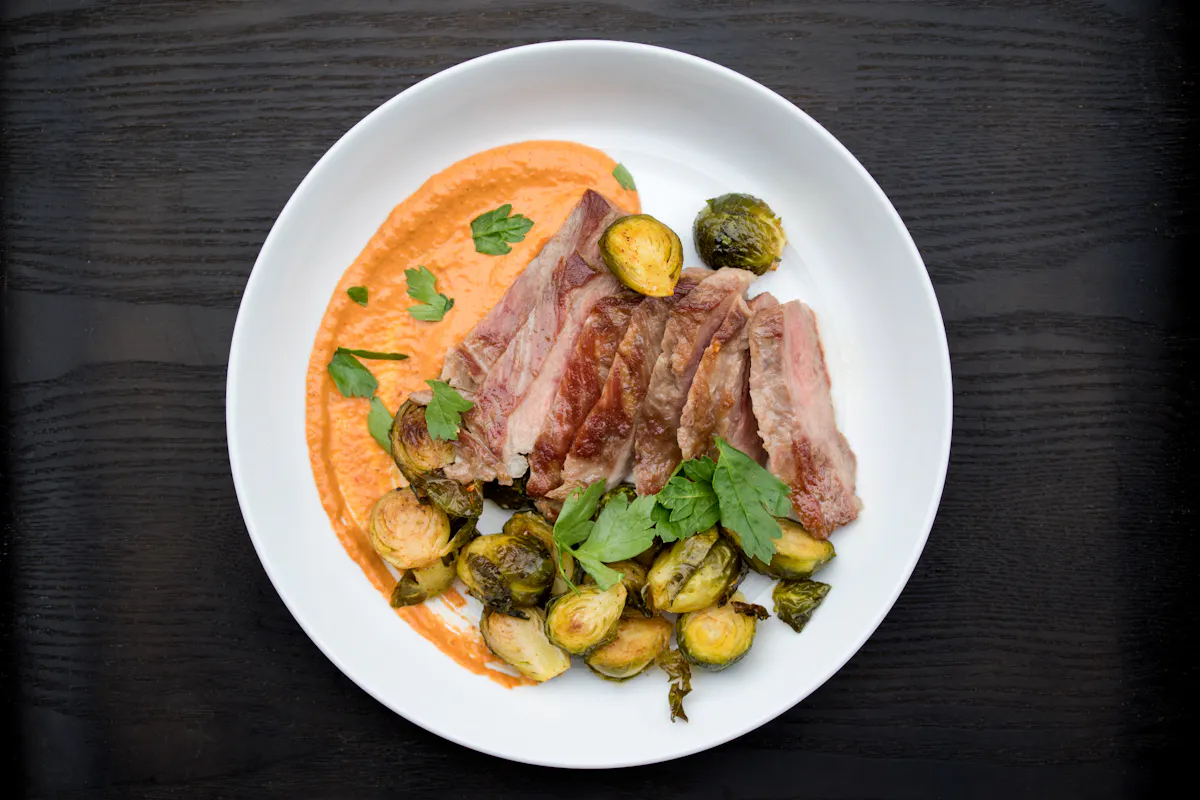 Sliced Ibérico pork pluma with romesco sauce and roasted Brussels sprouts