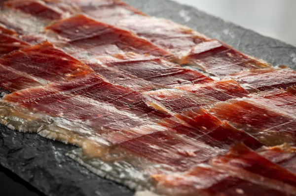 Paper-thin slices of Ib&eacute;rico jam&oacute;n laid in overlapping rows on dark slate