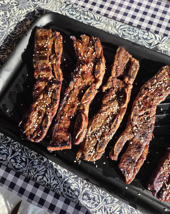 Four grilled kalbi-style beef short ribs with sesame seeds on a black tray