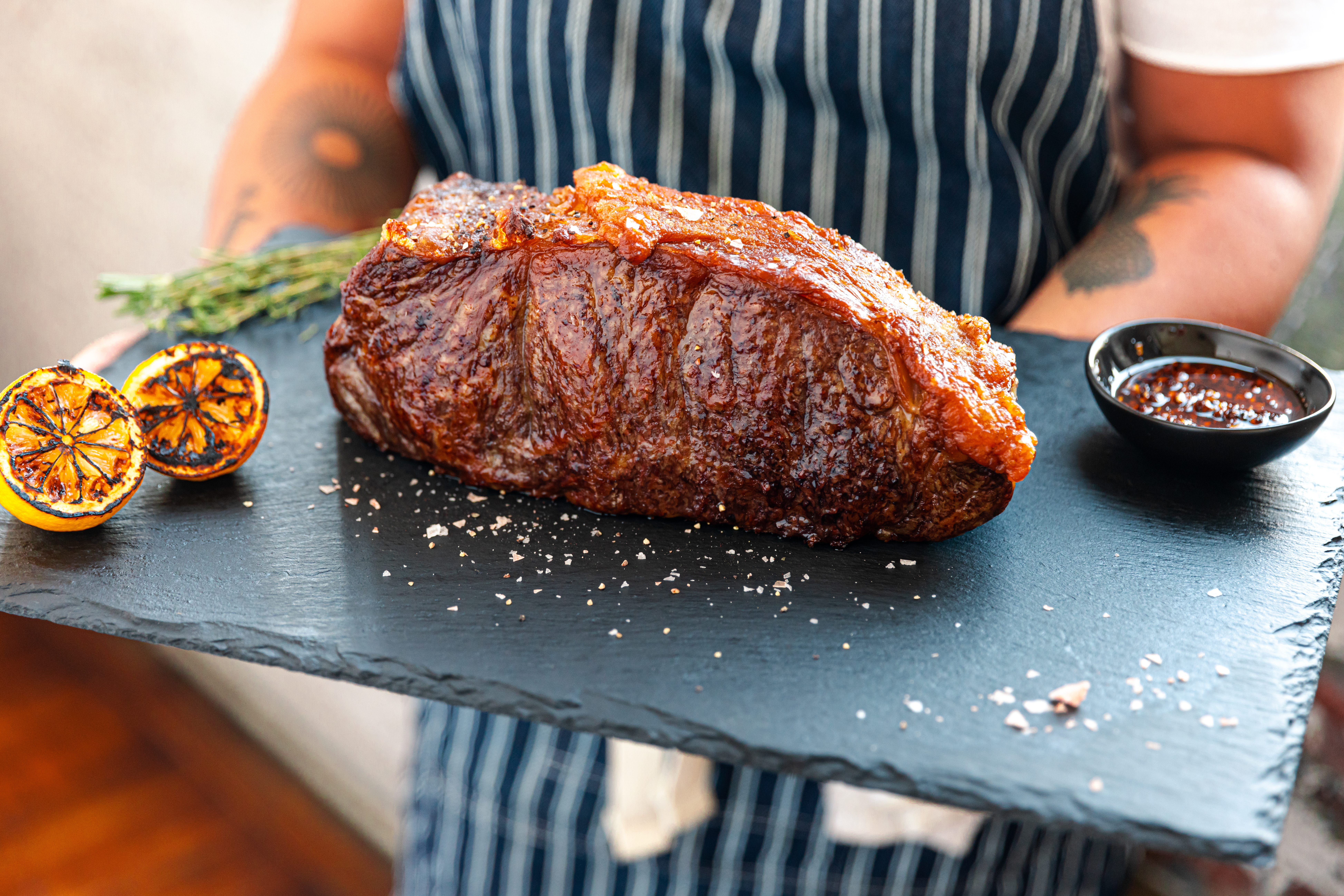 A cooked A5 Wagyu roast served on a slate platter with grilled citrus and a bowl of sauce