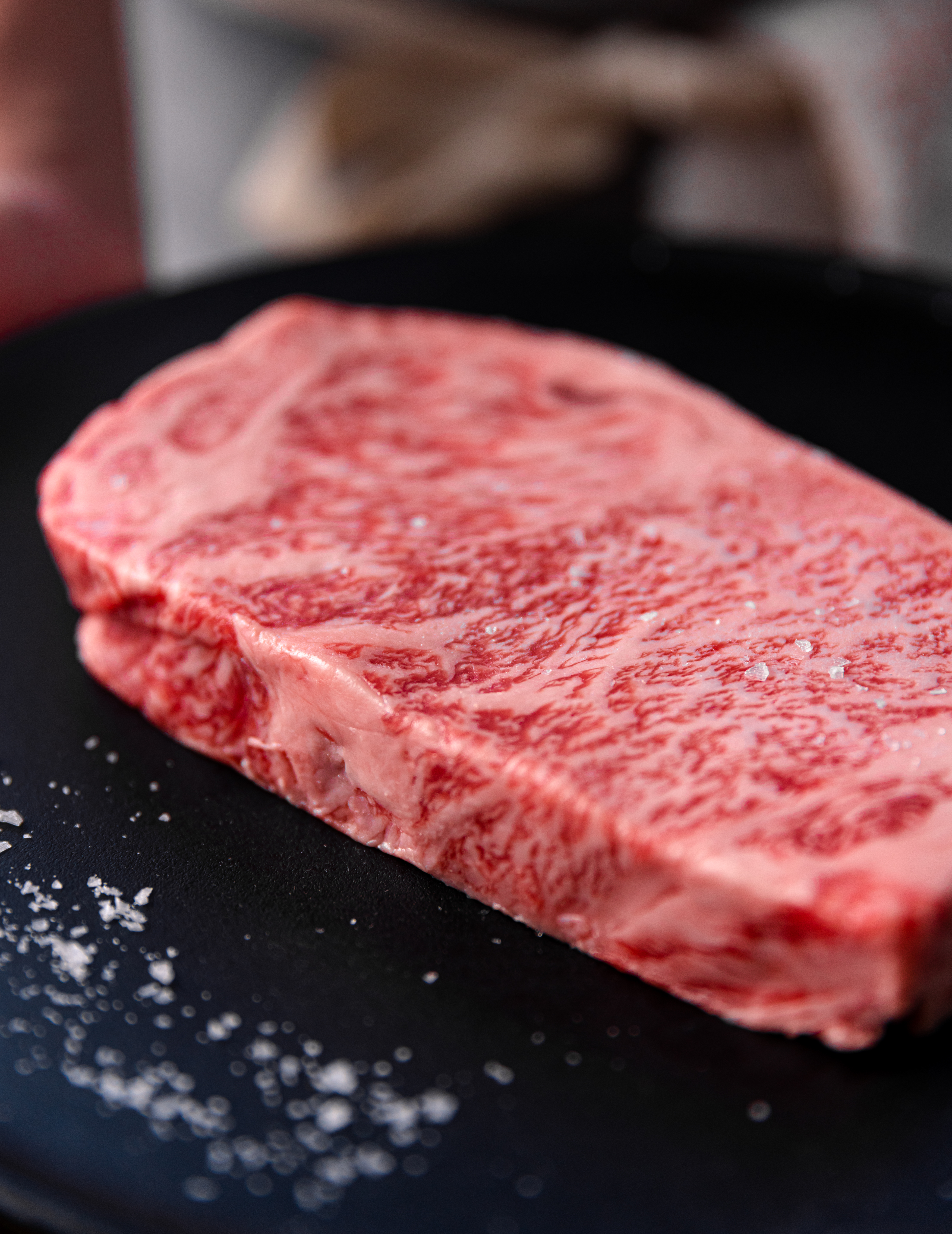 A raw, heavily marbled A5 Wagyu New York strip steak resting in a skillet with coarse salt