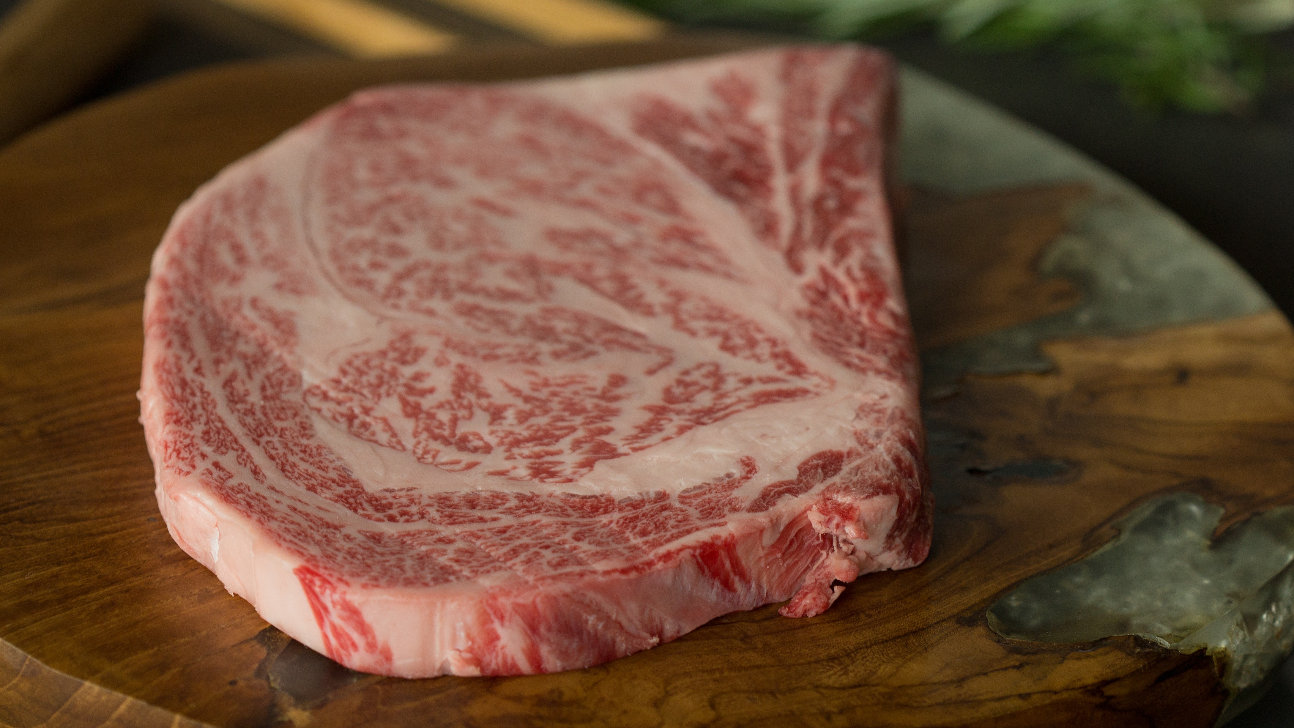 A raw Japanese A5 Wagyu ribeye steak with heavy marbling on a wooden board