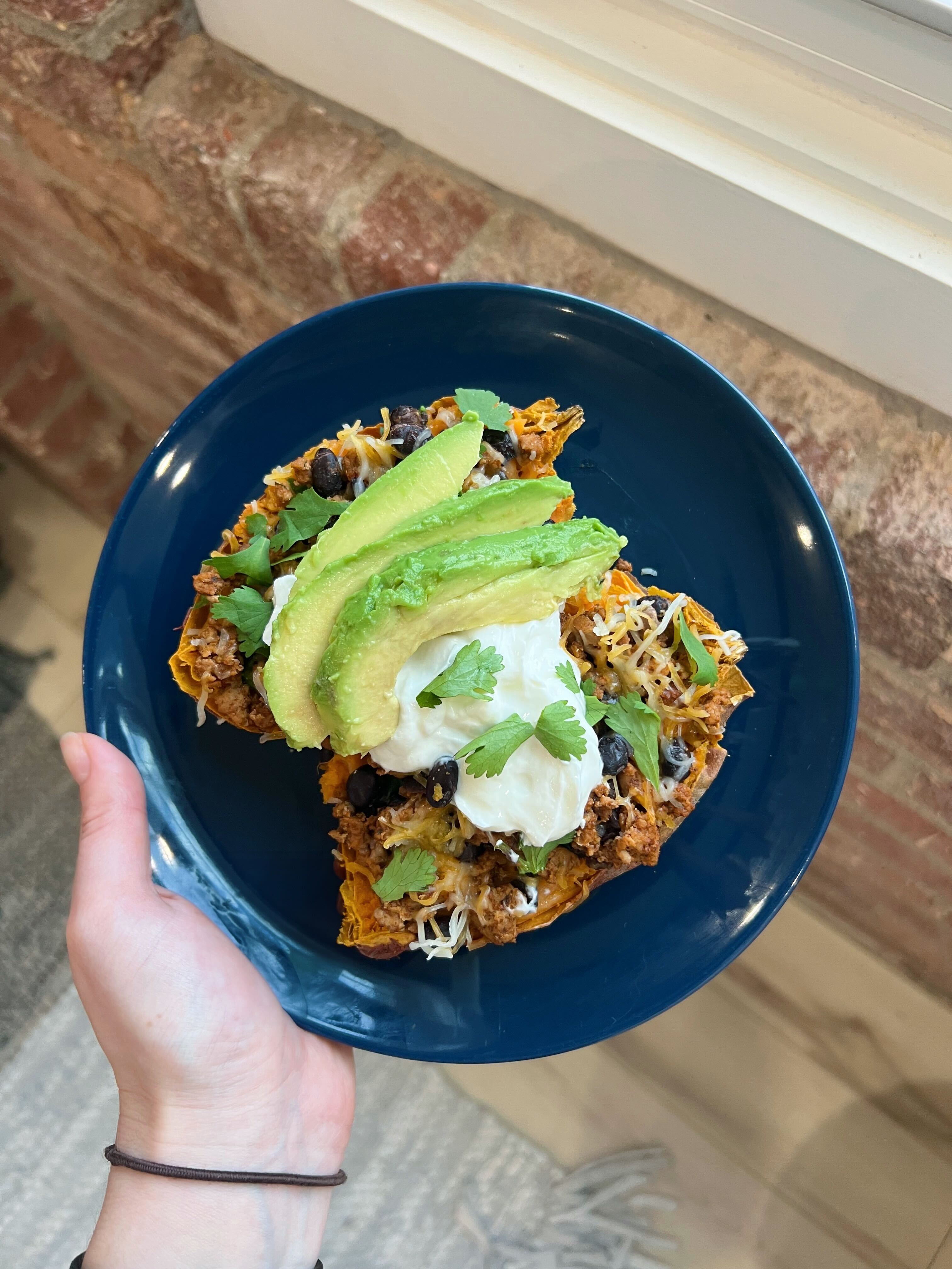 A loaded sweet potato topped with taco-seasoned ground turkey, avocado and sour cream