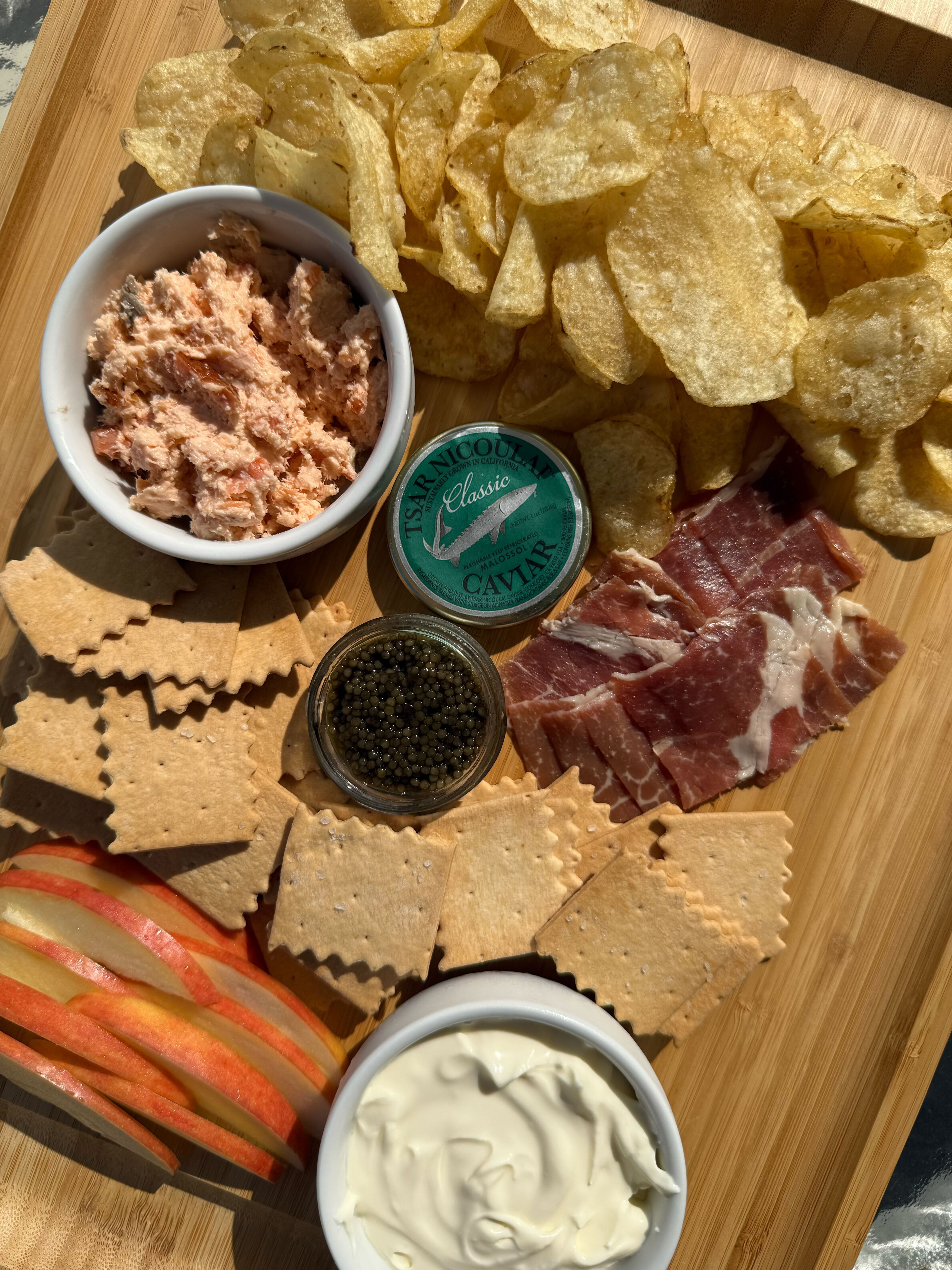 A charcuterie board with Ib&eacute;rico ham, smoked salmon spread, caviar, crackers and apples