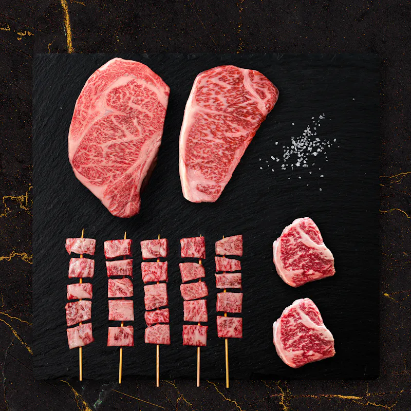 A5 Wagyu striploin steaks and skewers on a black slate board