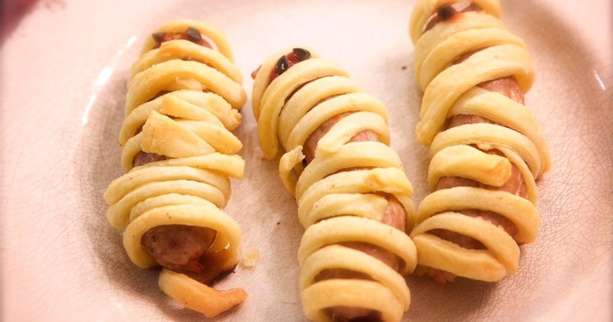 Sausage links wrapped in strips of dough to look like mummies, on a plate