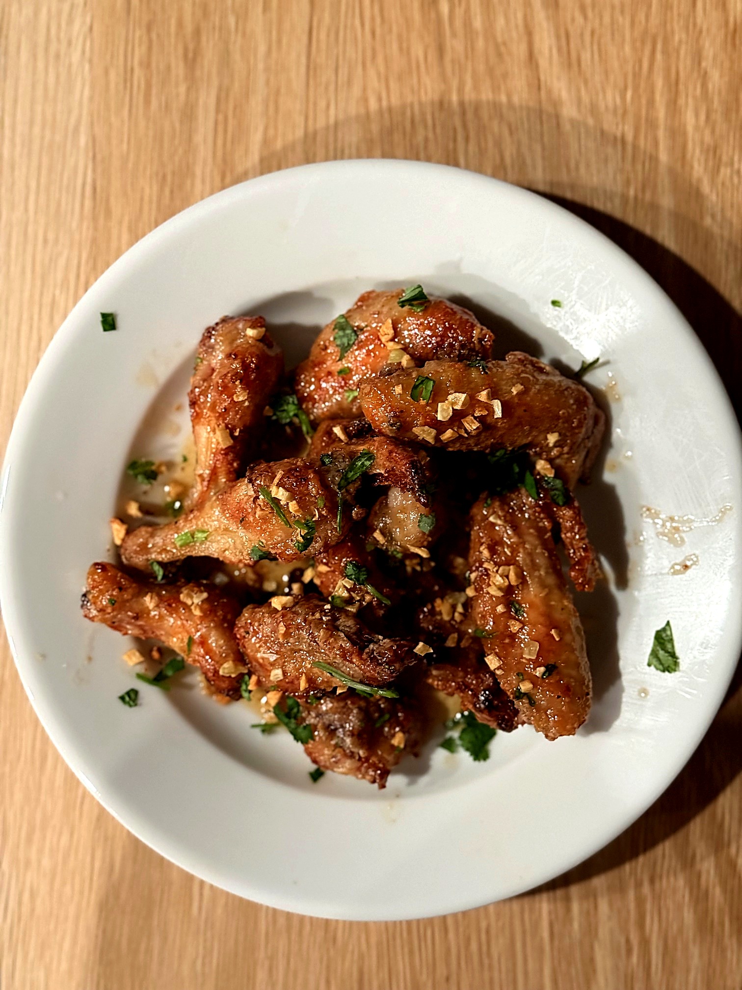 A white plate of glossy fish sauce chicken wings topped with fried garlic and cilantro