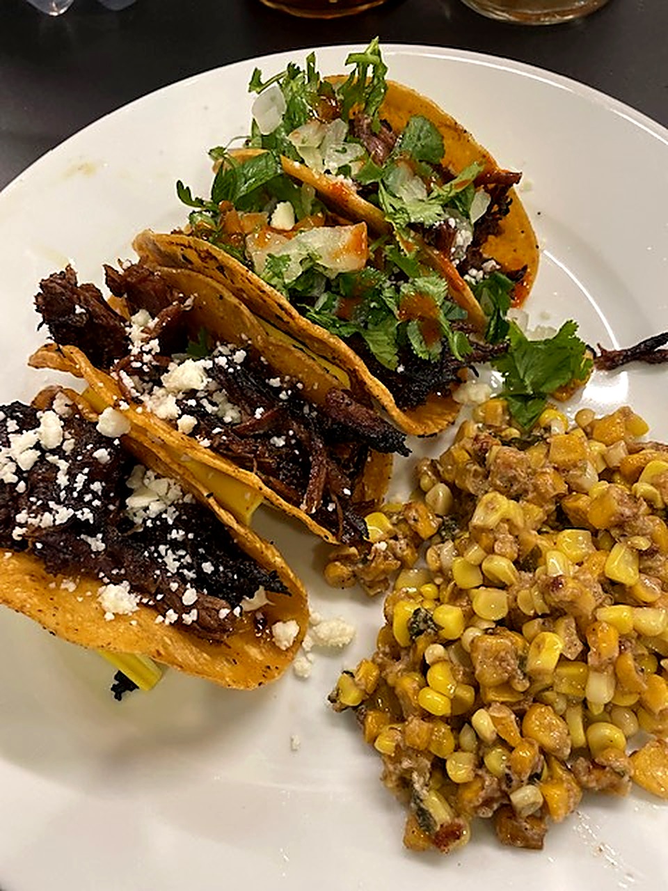 Crispy tacos filled with braised chuck roast, cotija and cilantro beside street corn