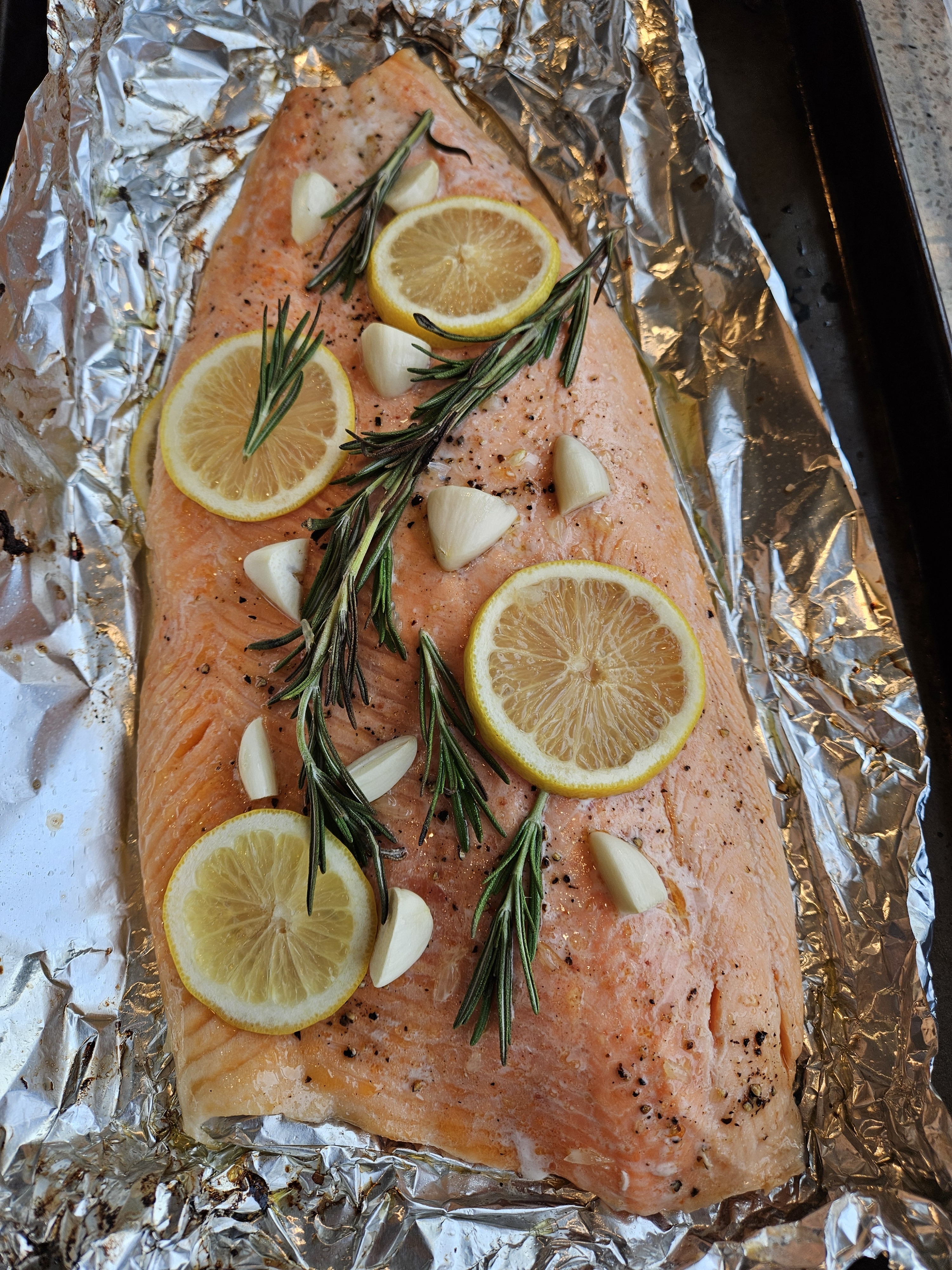 A whole side of Ōra King salmon baked in foil with lemon slices, rosemary and garlic