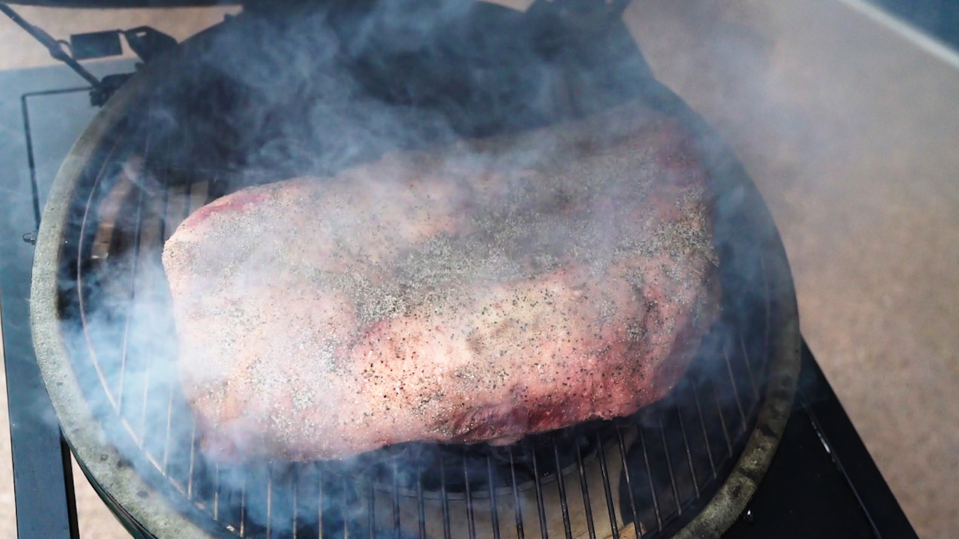 A seasoned beef brisket smoking on a grill, surrounded by heavy smoke