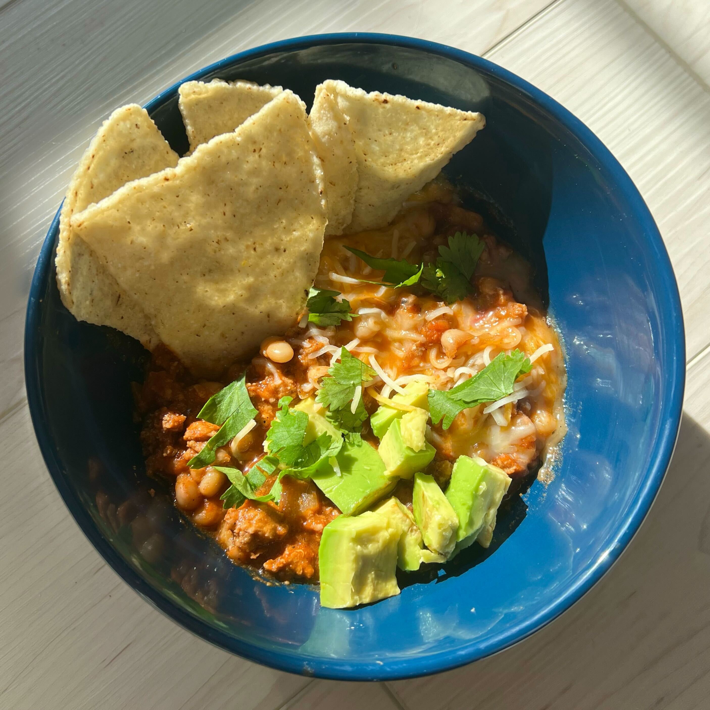 A bowl of turkey chili topped with avocado and cilantro, with tortilla chips