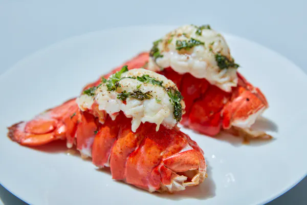Two baked lobster tails with herb butter on a white plate