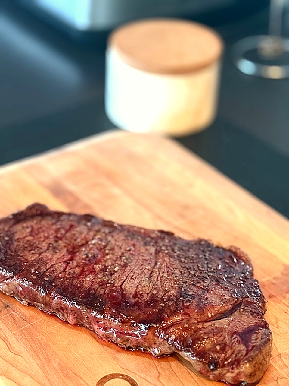 A seared New York strip steak with a dark crust resting on a wooden cutting board