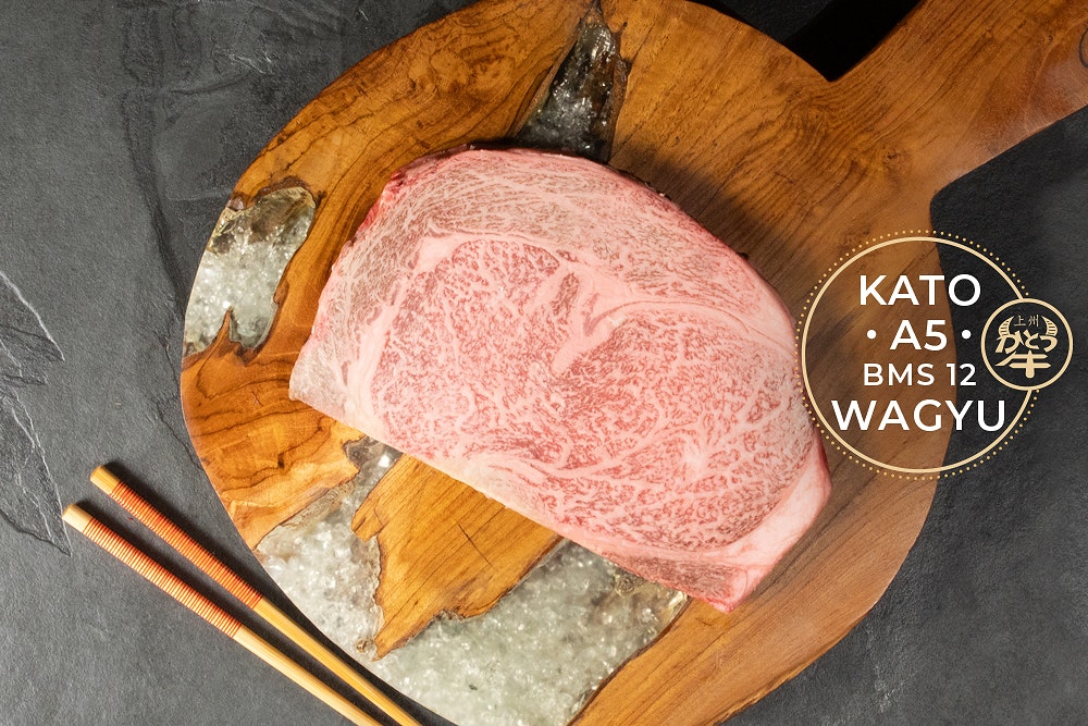 Raw Kato A5 BMS 12 wagyu steak, heavily marbled, on a wooden serving board with chopsticks