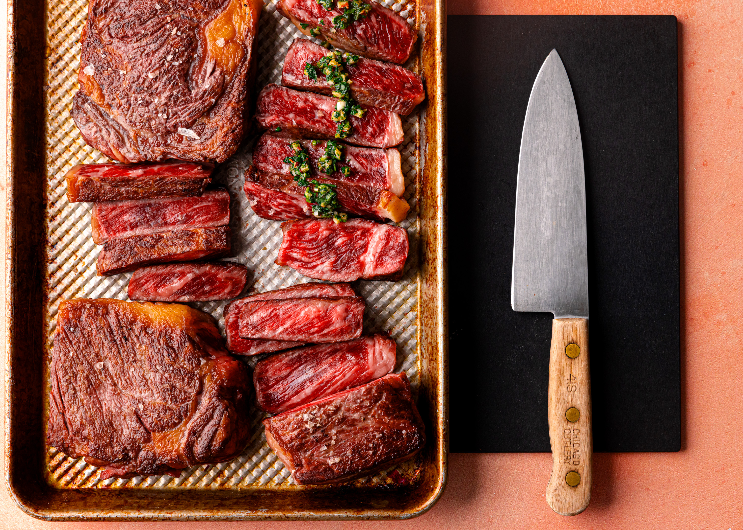 Sliced medium-rare flat iron steak topped with chimichurri on a sheet pan