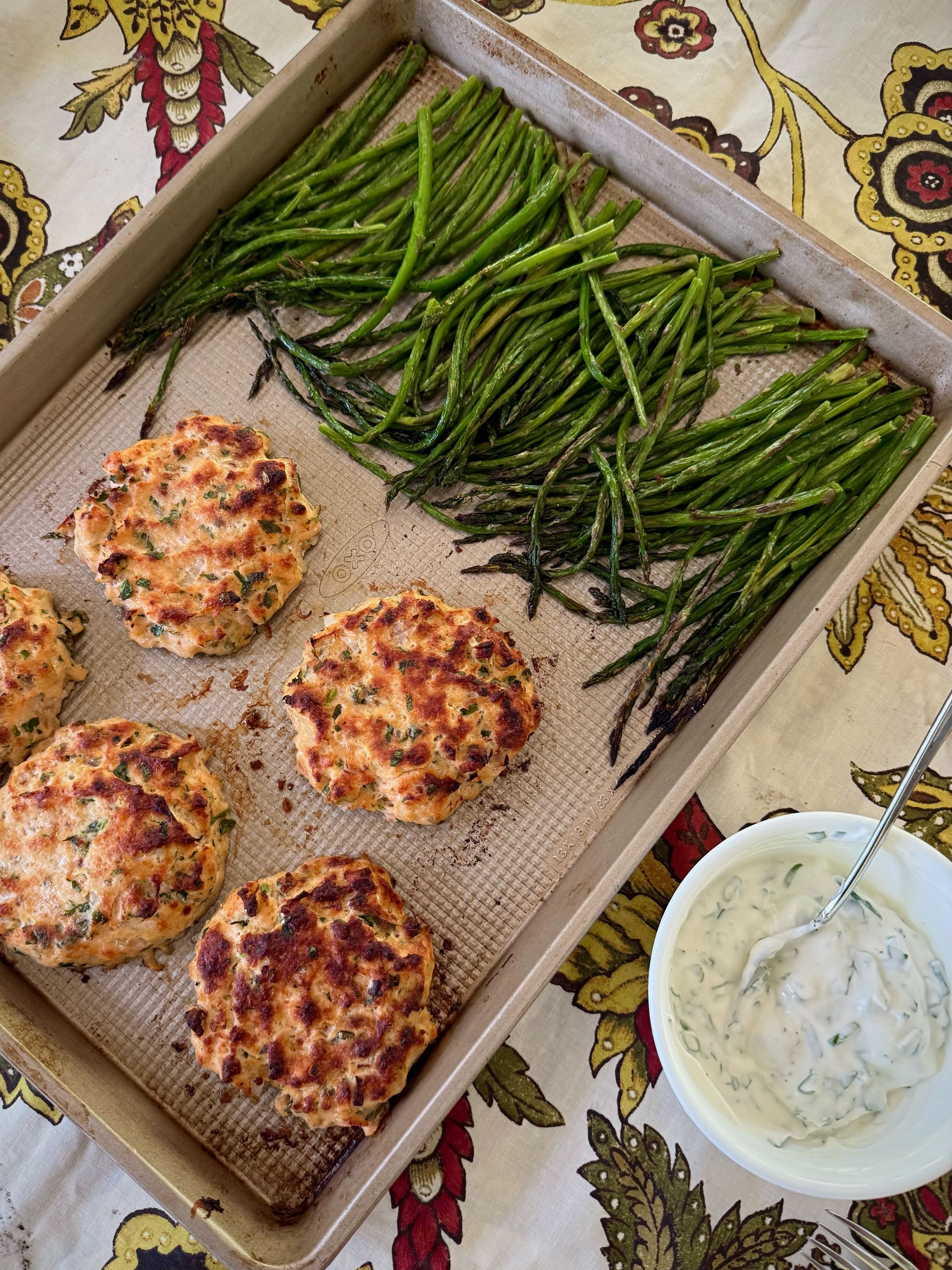 Golden salmon cakes on a sheet pan with roasted asparagus and a lemon herb sauce