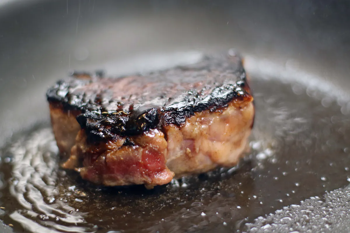A thick Ib&eacute;rico pluma searing in a hot pan with a dark crust