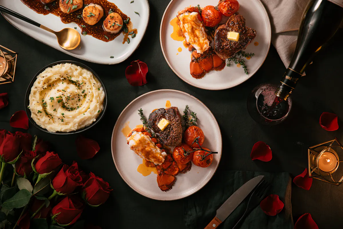 Plated lobster tail and steak dinners with mashed potatoes on a candlelit table