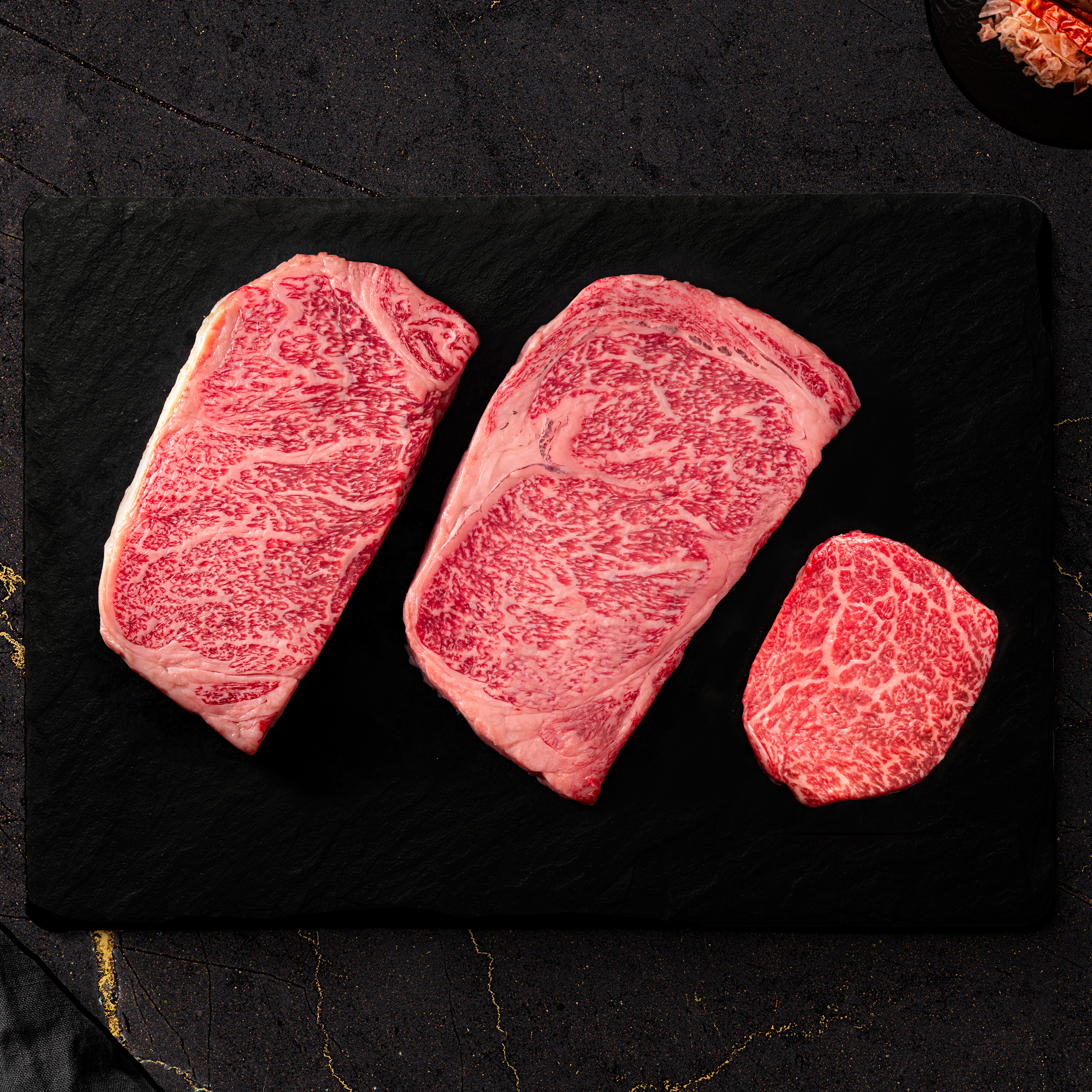 Three heavily marbled Japanese A5 Wagyu steaks arranged on a black slate board