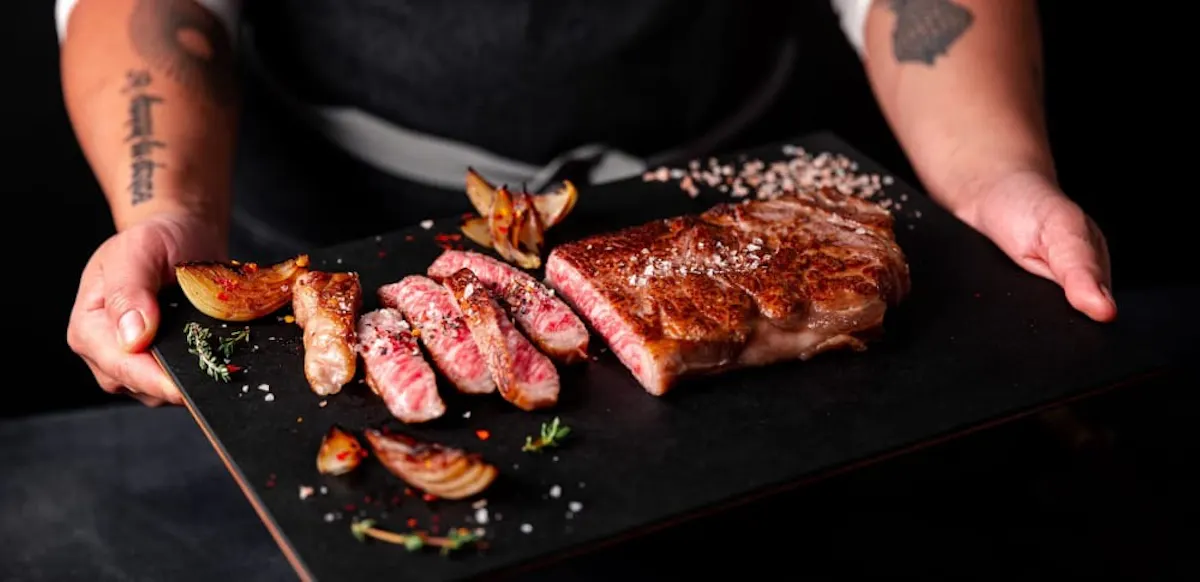 Sliced A5 Olive Wagyu New York strip on a dark serving board with roasted onions