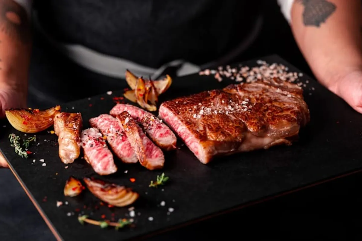 Sliced A5 Olive Wagyu New York strip on a dark serving board with roasted onions