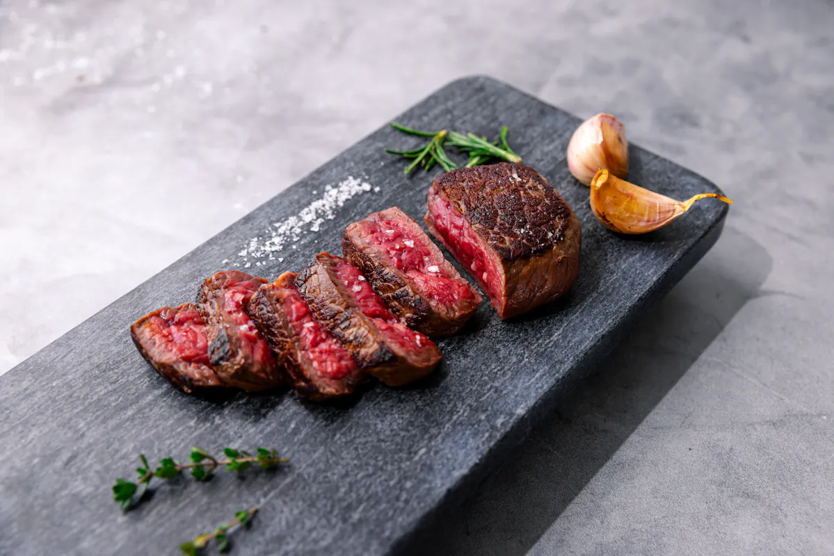 A seared Wagyu steak sliced medium-rare on a slate board with rosemary, thyme and roasted garlic