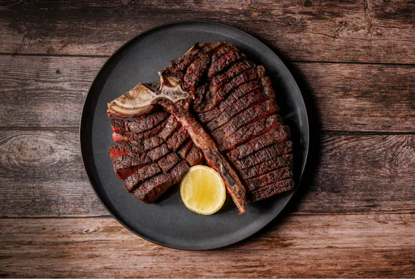Sliced T-bone steak on a black plate with a lemon wedge