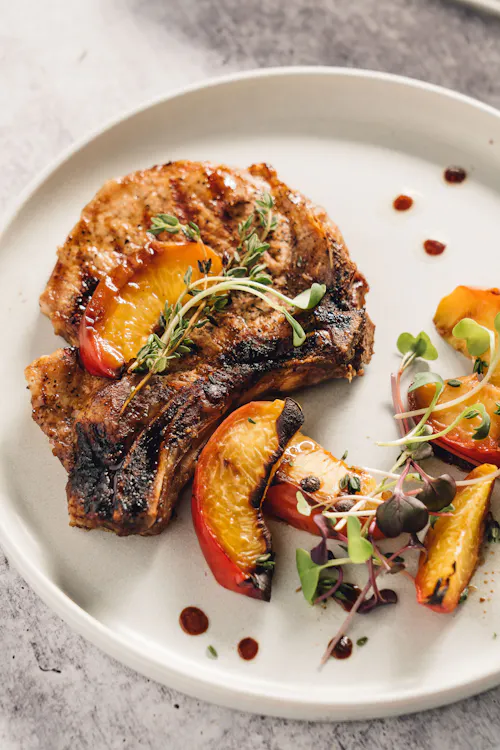 A grilled bone-in pork chop plated with stone fruit