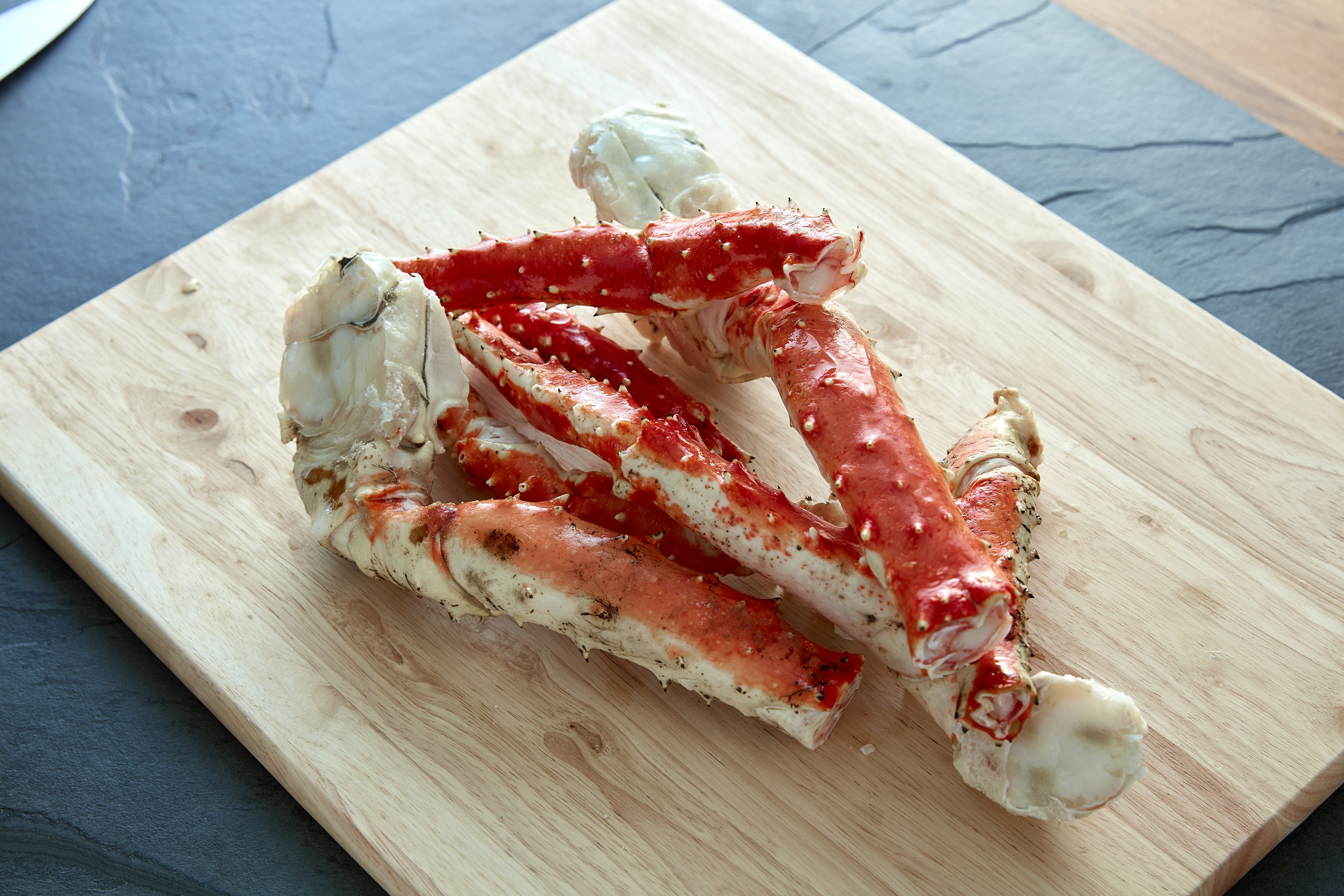 Red king crab legs stacked on a wooden cutting board